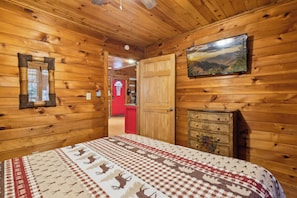 Een houten interieur met een bed, een televisie en een rode deur naar een andere kamer.