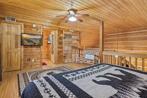 A wooden cabin interior with a bed, a television, a ceiling fan, and a view of the outdoors. - 2BR Getaway with Hot Tub, Firepit & Outdoor TV Fun! (Gatlinburg)