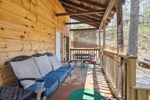 A wooden cabin with a covered porch, a sofa with cushions, a metal table, and a chair. - 2BR Getaway with Hot Tub, Firepit & Outdoor TV Fun! (Gatlinburg)