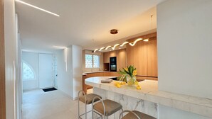 Una cocina moderna con encimera de mármol, dos taburetes de bar y un florero con flores amarillas.