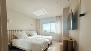 Habitación de hotel moderna con una cama grande, una mesita de noche, un espejo y vistas al mar a través de la ventana.