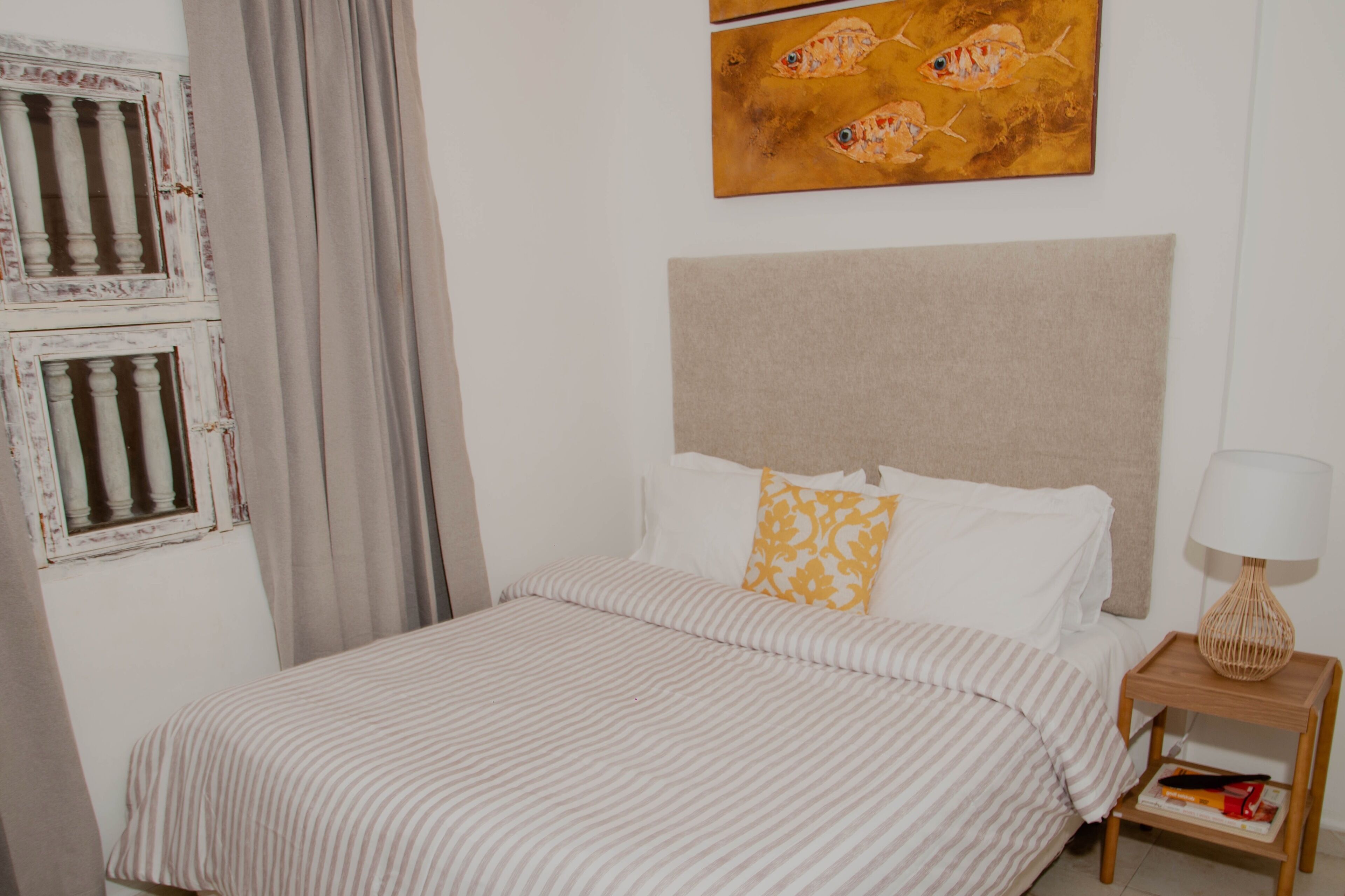 A neatly made bed with striped bedding, a headboard, and a bedside table with a lamp.