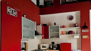 A compact kitchen with red cabinets, a white refrigerator, a microwave, and a gas stove. - Cozy and quiet apartment in ideal location in Reggio Cal. (Reggio Calabria)