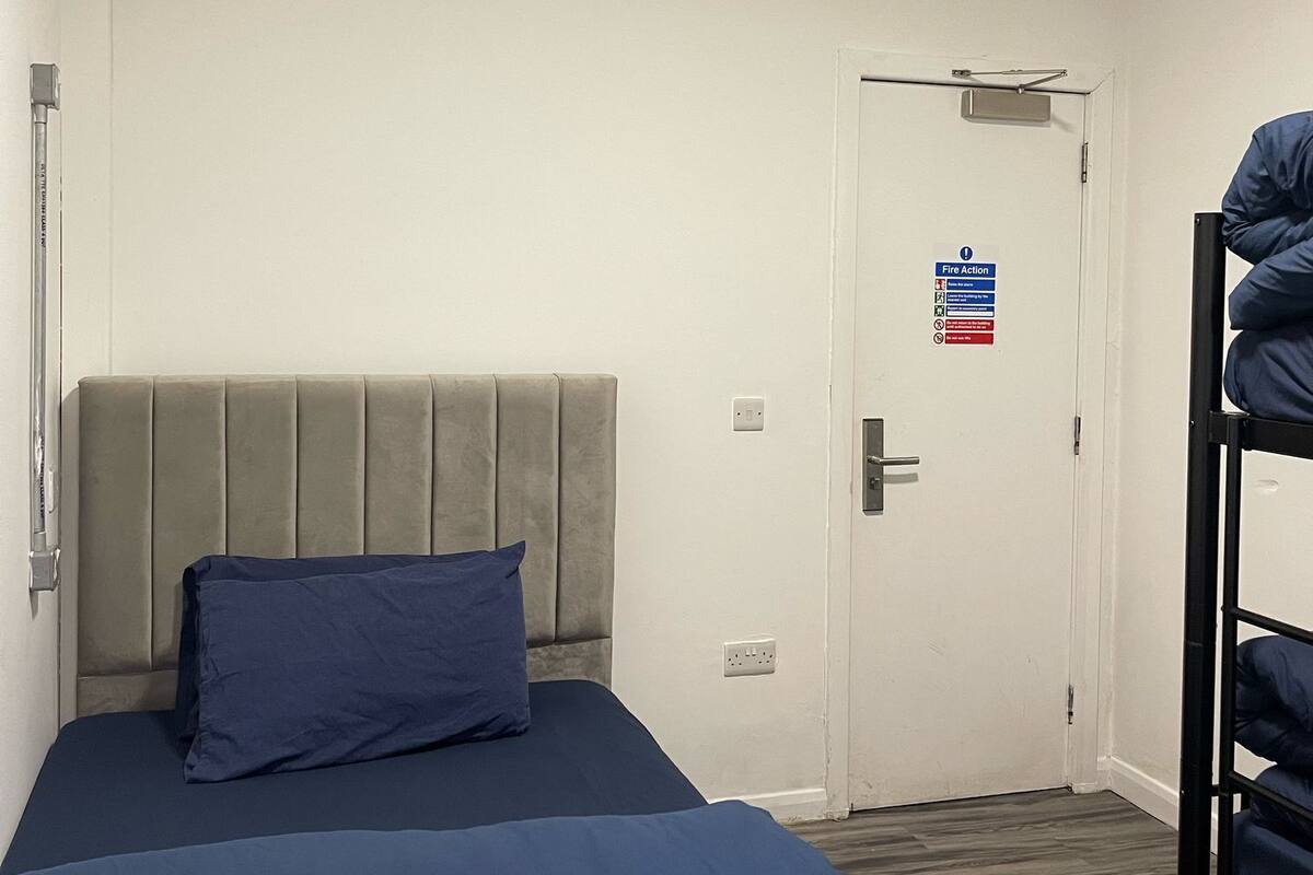 Habitación de hotel con cama, literas, una puerta con señal de evacuación por incendio y una lámpara en el techo.