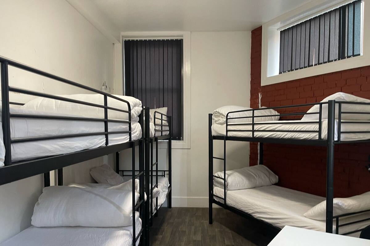 Un dormitorio con literas, una ventana con persianas, una pared de ladrillo y una mesa blanca.