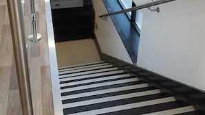 En modern inredning med en trappa, ett glasräcke och färgglada stolar vid ett fönster.