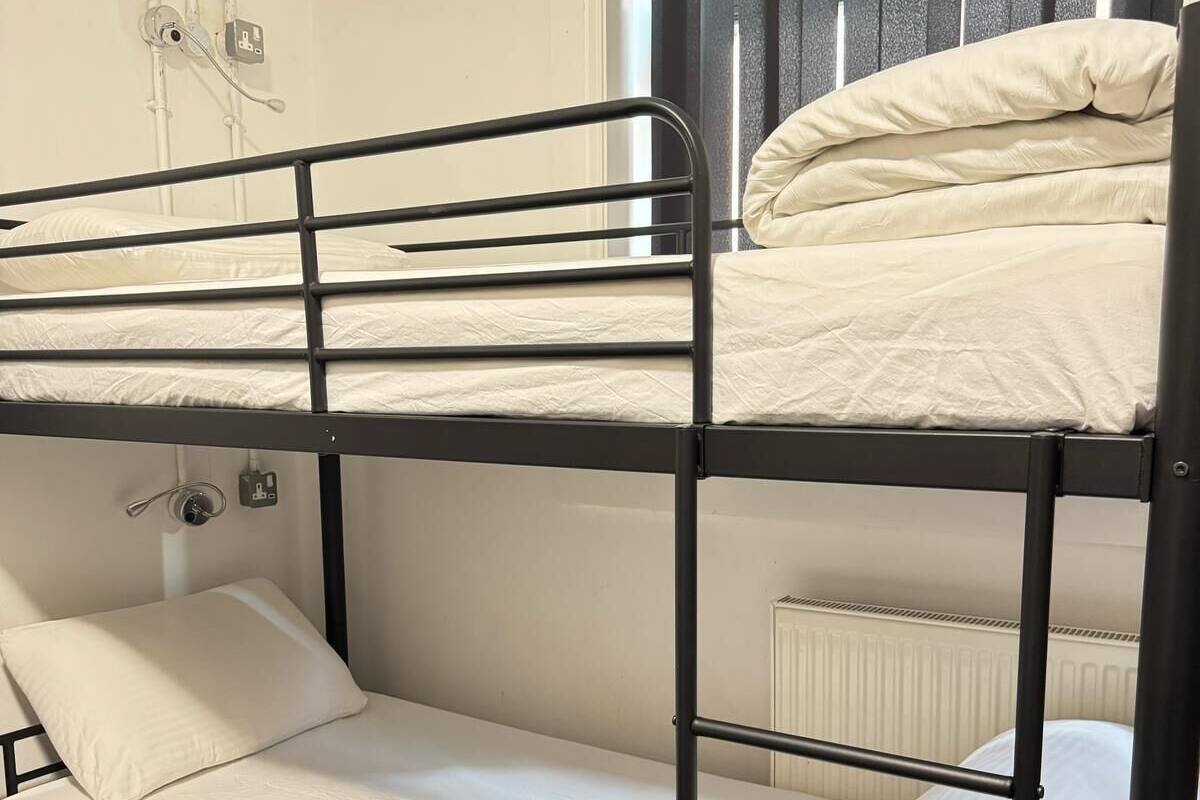 Una cama litera con colchón y almohadas, una ventana con persianas y un radiador.