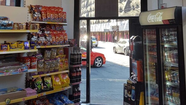En butiksinredning med ett Coca-Cola-kylskåp, hyllor med snacks och en kristallkrona.
