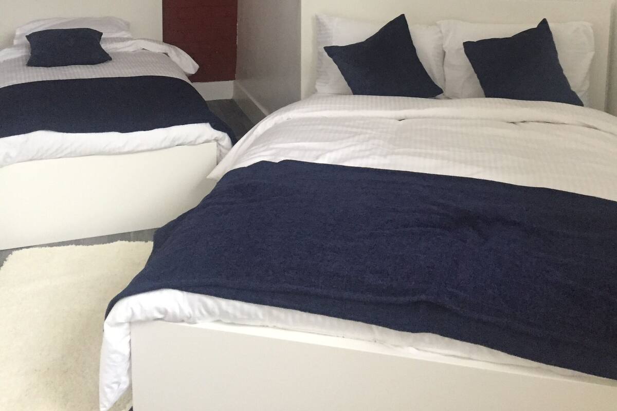 Un dormitorio con dos camas, ropa de cama blanca y una pared de ladrillo.