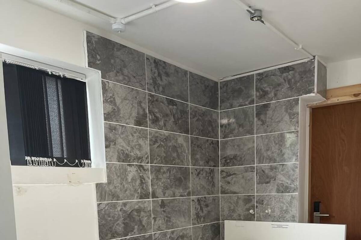 Un dormitorio pequeño y moderno con dos camas individuales, una ventana con cortinas y un revestimiento de ducha de azulejos.