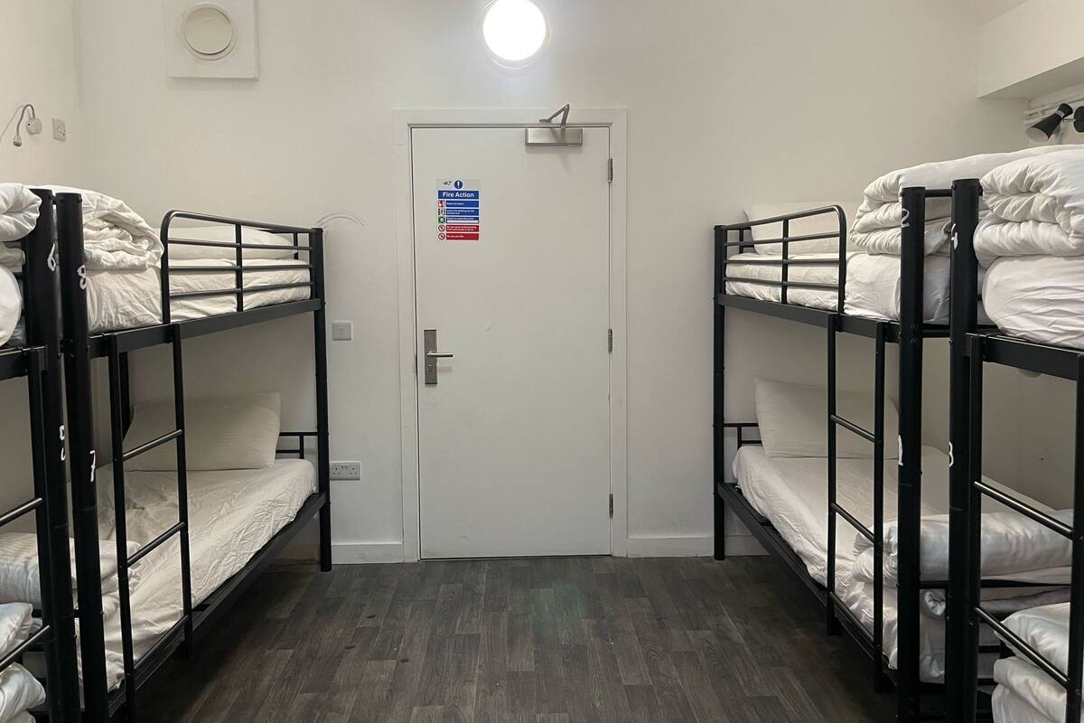 Un dormitorio con camas literas, una puerta con señal de evacuación y una lámpara sobre la puerta.