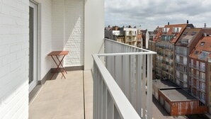 Ein Balkon mit weißer Brüstung, einem kleinen Tisch und Blick auf die Nachbargebäude.