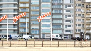 Ein mehrgeschossiges Wohngebäude mit Balkonen, einem verschlossenen Eingangsbereich und geparkten Fahrzeugen.