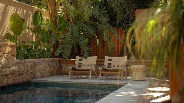 A poolside area with two wicker chairs, a stone wall, and lush greenery.