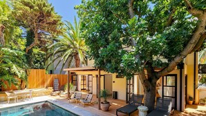 A poolside area with a wooden deck, lounge chairs, and a small table. - Botany House Boutique Retreat (Cape Town)