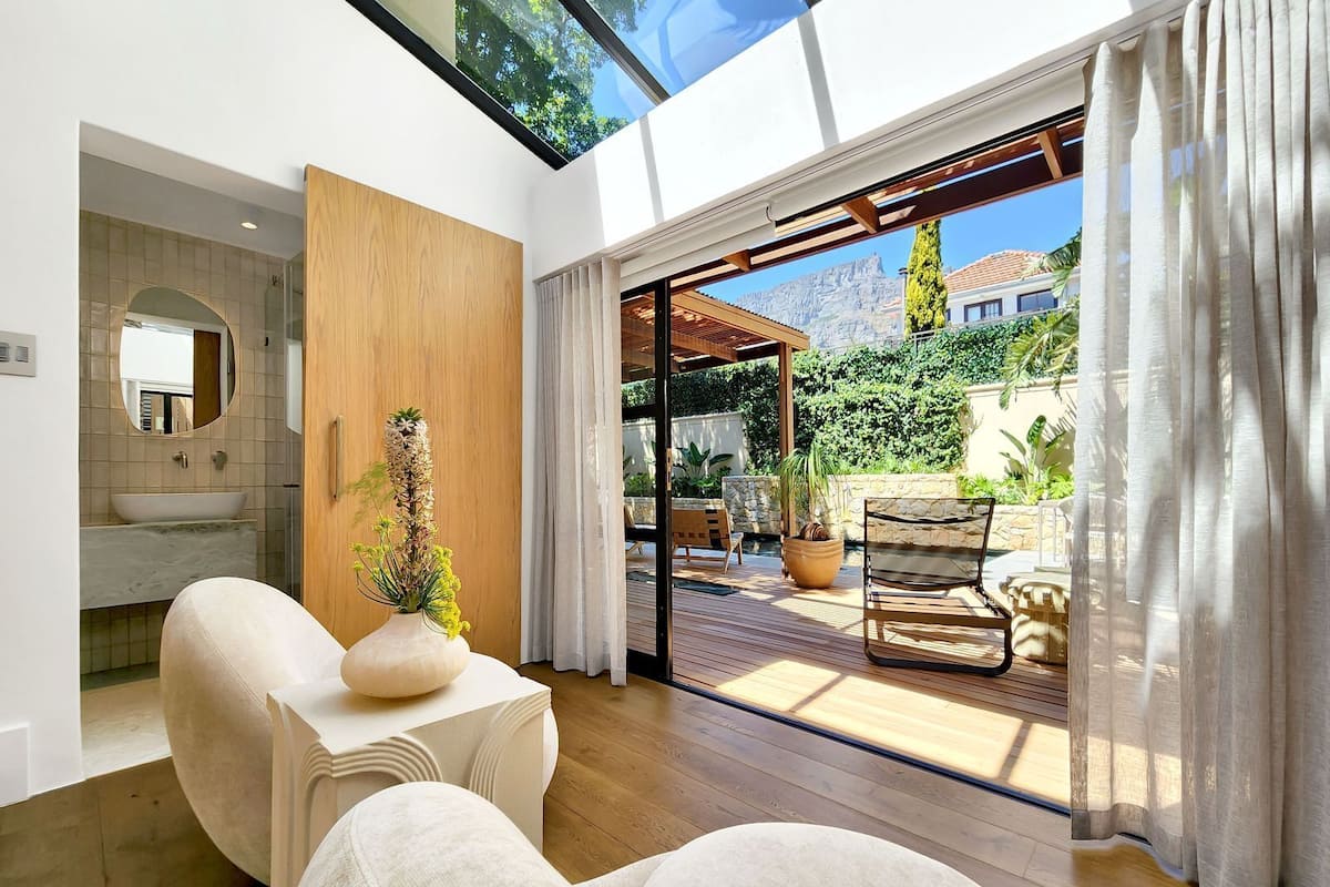 Um interior moderno com piso de madeira, uma janela grande e vista para um jardim e montanhas.