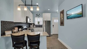 Una cocina moderna con una isla central, taburetes de bar, un refrigerador de acero inoxidable y un televisor de pantalla plana montado en la pared.