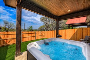 A hot tub with a wooden deck and a covered area, surrounded by a wooden fence and trees.