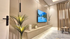 Ein modernes Wohnzimmer mit einem an der Wand befestigten Flachbildfernseher, einem Holzkonsolentisch mit Dekorationen, einer Zimmerpflanze und einem dunkelgrauen Sofa.