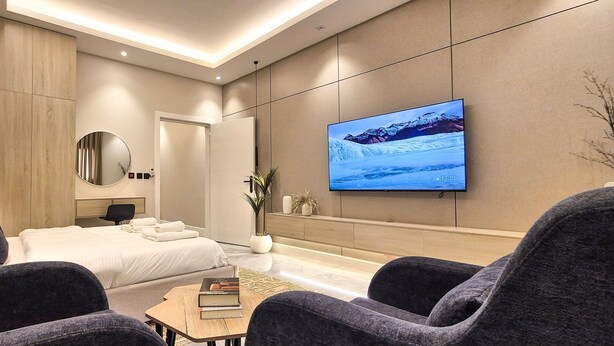 Ein modernes Hotelzimmer mit einem großen Bett, einem flachbildfernseher an der Wand, einem runden Spiegel und einer Sitzecke mit zwei Sesseln und einem kleinen Tisch.