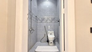 Ein kleines, abgeschlossenes Badezimmer mit Toilette, Dusche und einem Handtuch auf dem Boden.