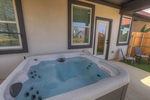 Un jacuzzi en un entorno exterior con una terraza de madera y una vista de una casa al fondo.