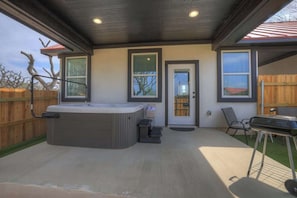 Ein überdachter Patio-Bereich mit Whirlpool, Grill und einer zur Haustür führenden Tür.
