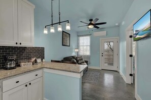A kitchen with white cabinets, a granite countertop, a ceiling fan, and a dining area with a couch and a TV. - Modern Casita w/Hot-Tub, Six Minutes from Main St! (Fredericksburg)