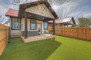 Ein modernes Haus mit überdachter Veranda, eingezäunter Hinterhof und gepflegtem Rasen.