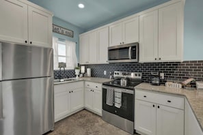 Una cocina moderna con armarios blancos, electrodomésticos de acero inoxidable y un salpicadero de azulejos negros.