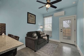 A room with a dining table, a sofa, a ceiling fan, a window with blinds, and a door.