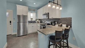 Una cocina moderna con armarios blancos, un refrigerador de acero inoxidable, un microondas e isla de granito con taburetes de bar.
