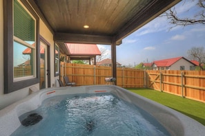 Ein Whirlpool unter einer Holzpergola mit Blick auf einen Garten und angrenzende Häuser.