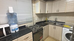 Een kleine keuken met een magnetron, waterdispenser, fornuis, spoelbak en wasmachine.