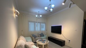 Een moderne woonkamer met een bank, een salontafel, een aan de muur bevestigde televisie en een plafondlamp.