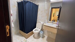 Een badkamer met douchegordijn, toilet, wastafel en een prullenbak.