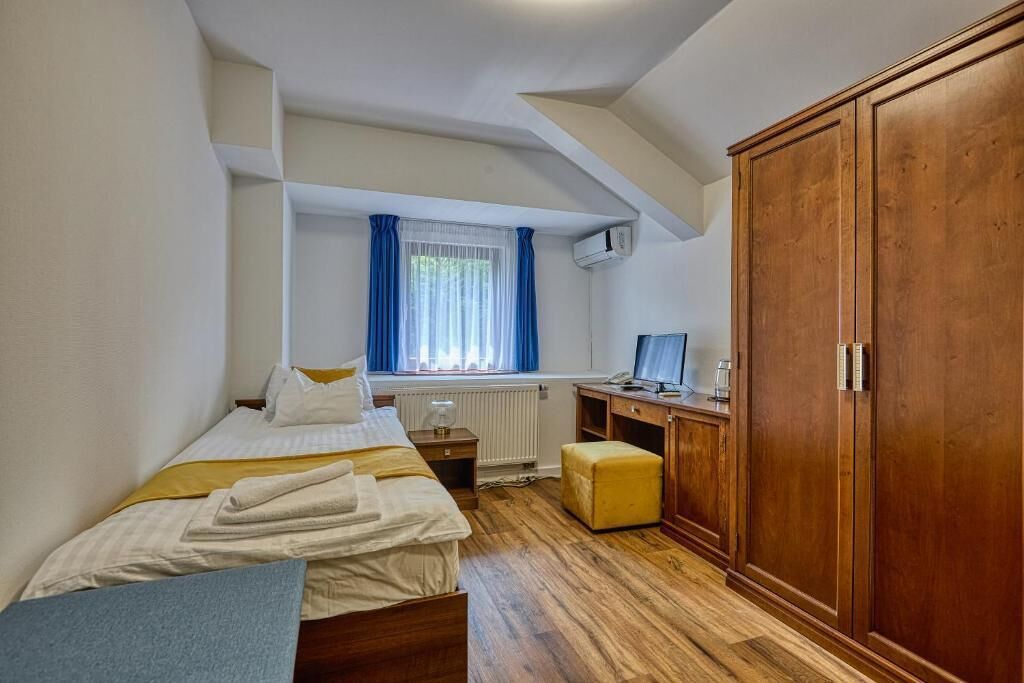 Un dormitorio con cama, escritorio, armario y ventana con cortinas.