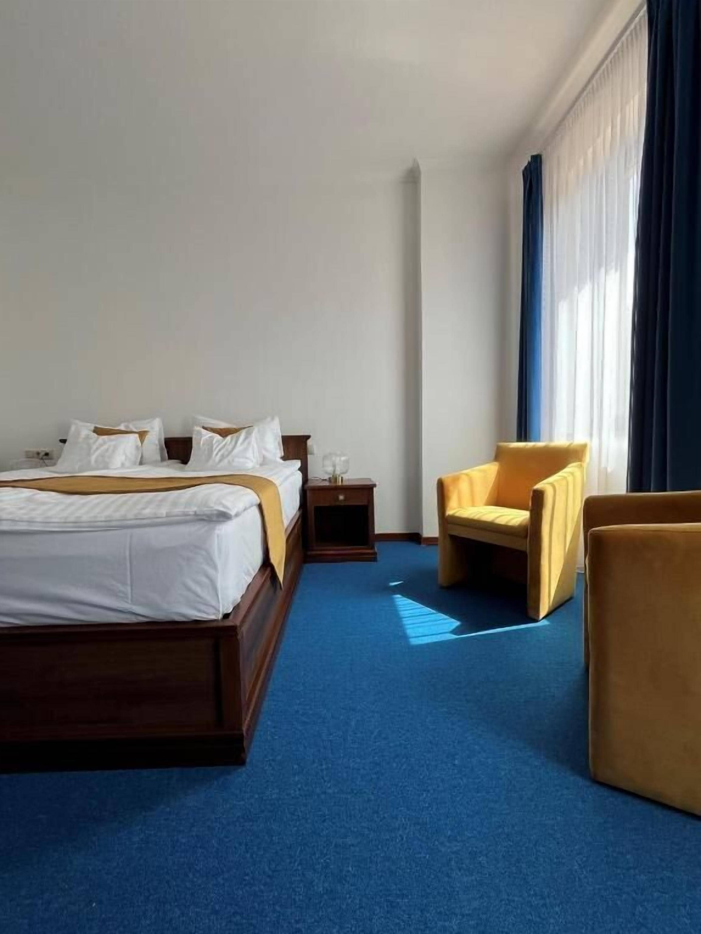 A hotel room with a large bed, a bedside table, a chair, and a window with curtains.
