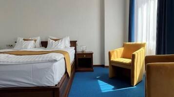 A hotel room with a large bed, a bedside table, a chair, and a window with curtains.