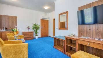 Habitación de hotel con alfombra azul, muebles de madera, un televisor de pantalla plana, un escritorio con teléfono y una planta en maceta.