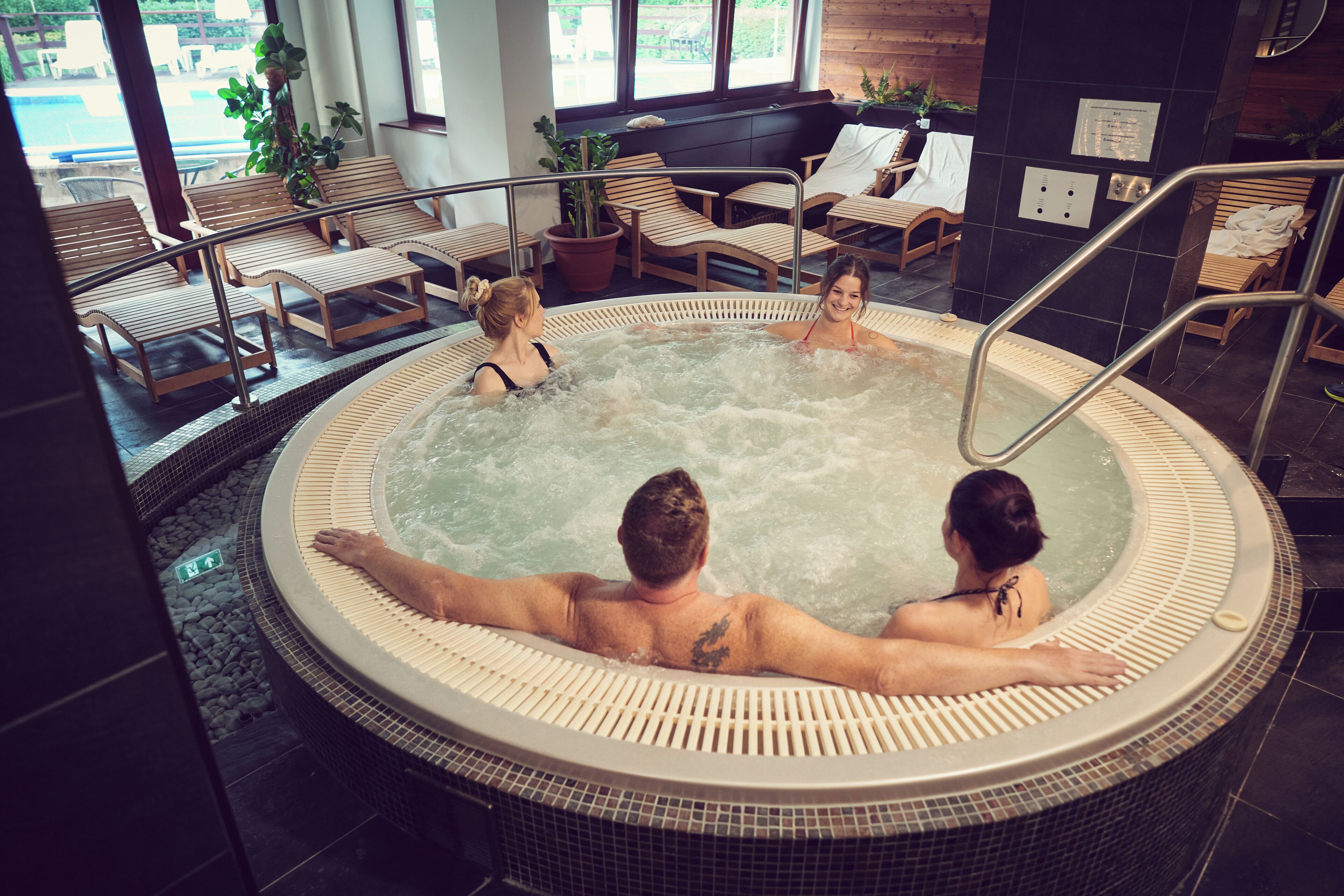 Un jacuzzi con tres personas, rodeado de sillones de descanso y una piscina.