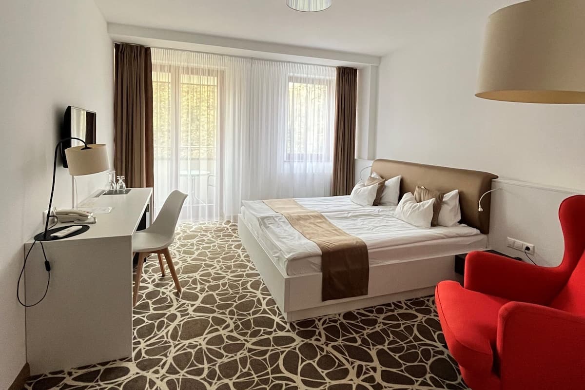 A hotel room with a bed, a desk, a chair, and a red armchair.