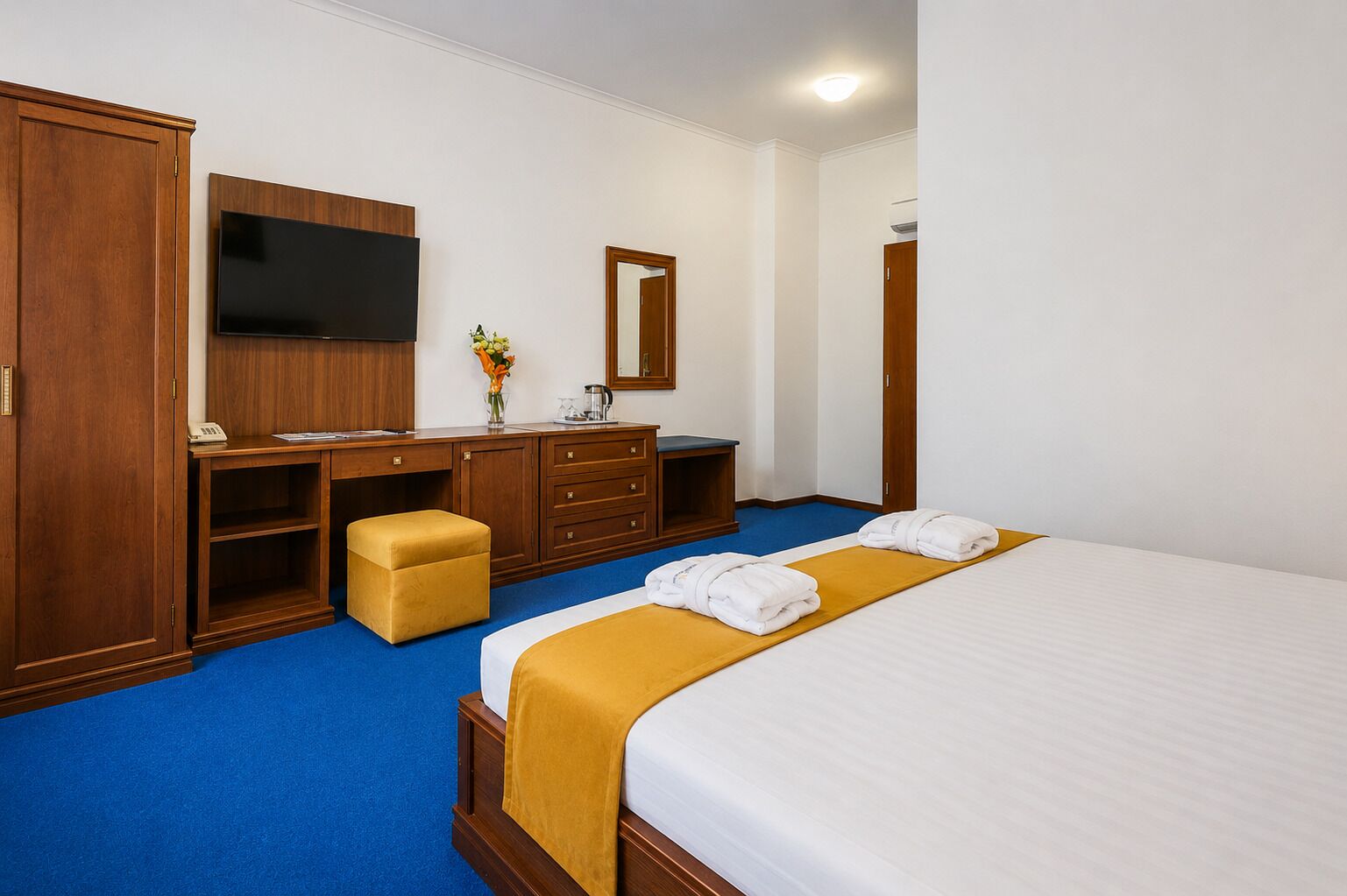 Quarto de hotel com cama, secretária, televisão de tela plana, guarda-roupa e espelho.