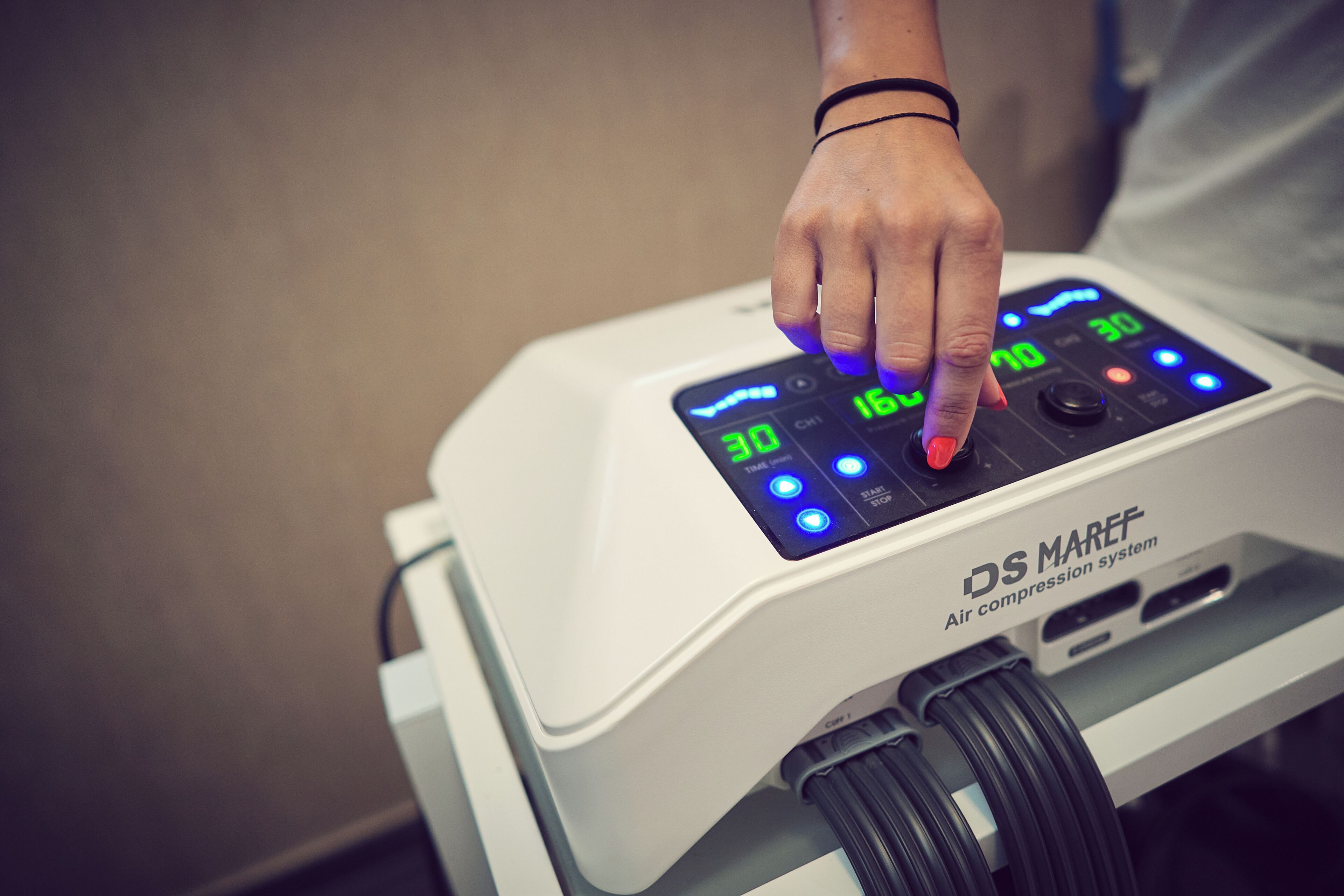Una mano presionando un botón en un dispositivo médico con pantallas digitales y una etiqueta que dice 'DS MAREF Sistema de compresión neumática'.