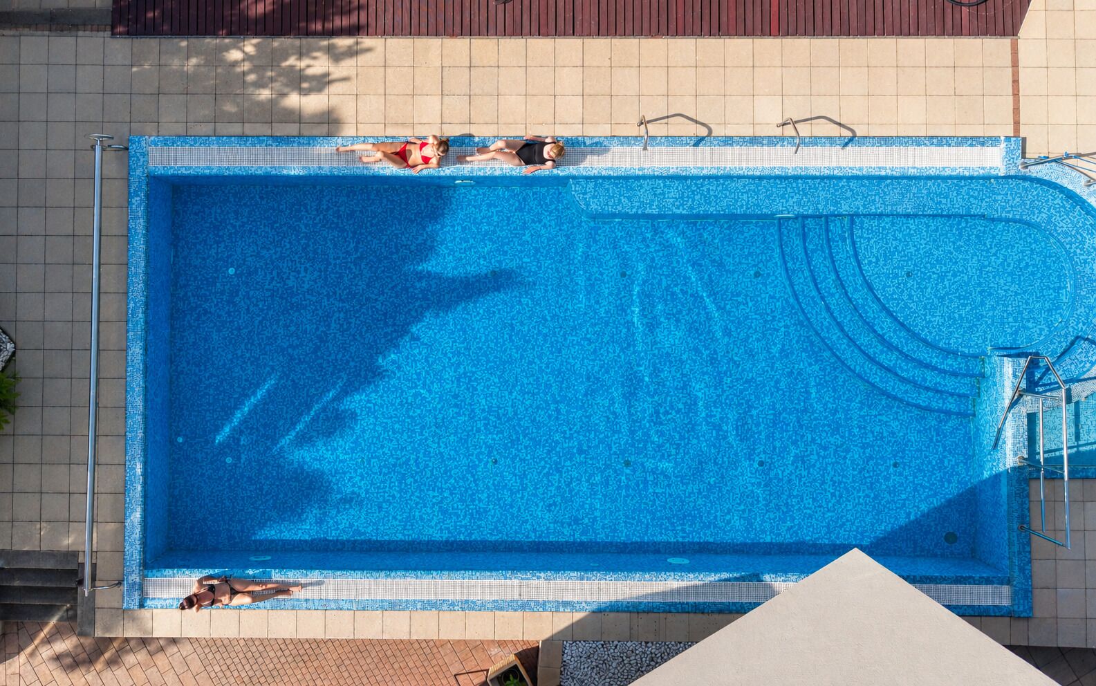 Una piscina rectangular con borde de azulejos, una escalera y una zona de solárium con baldosas.