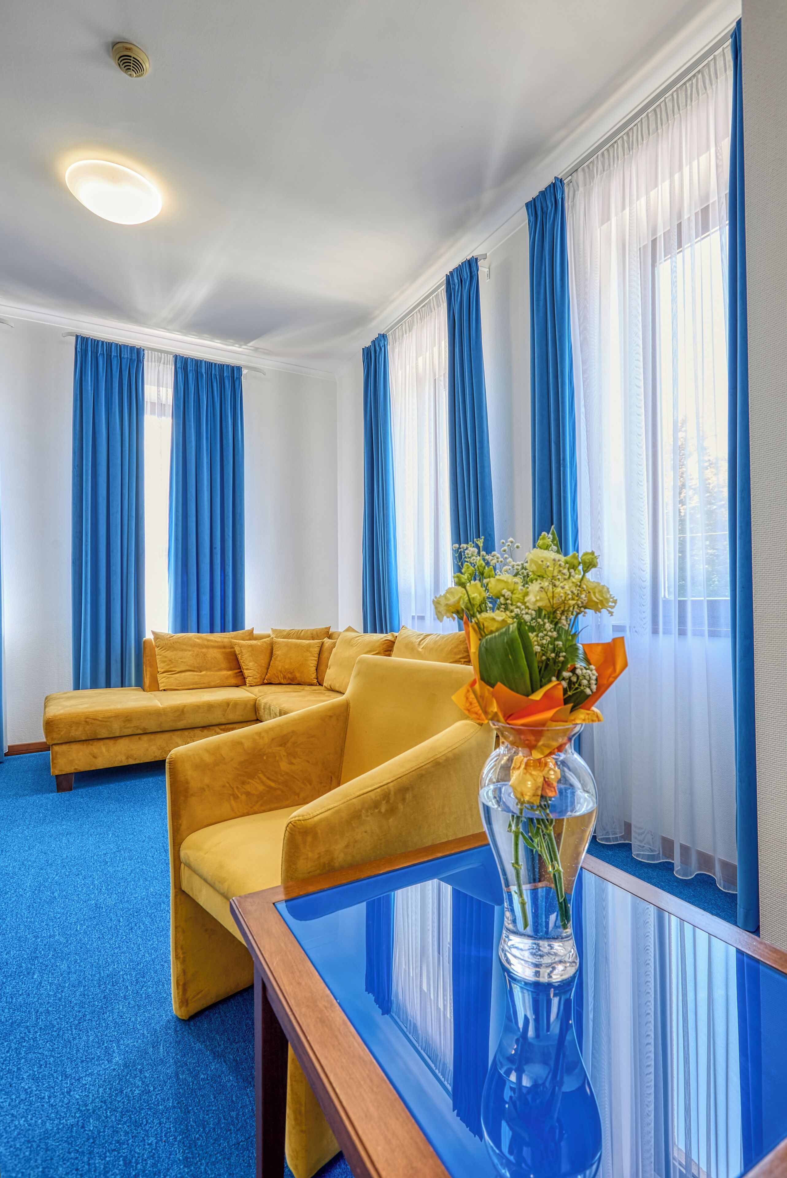Una habitación con un sofá seccional, una mesa de centro de vidrio y un jarrón con flores.