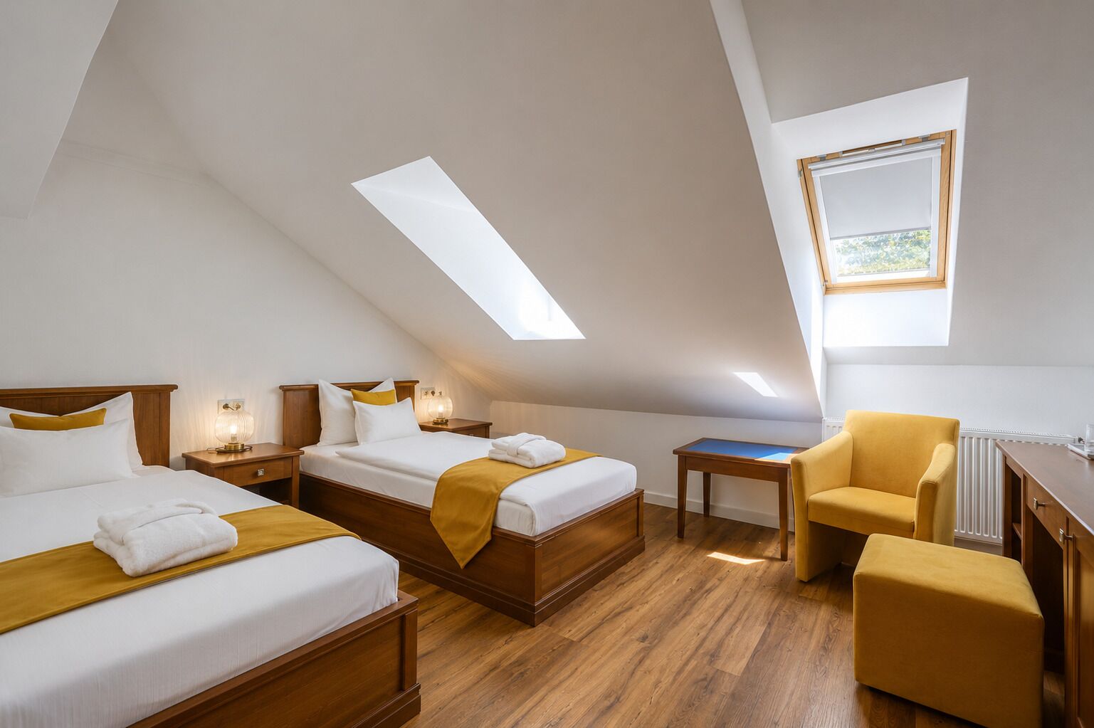 A hotel room with two beds, a desk, a chair, and a skylight.