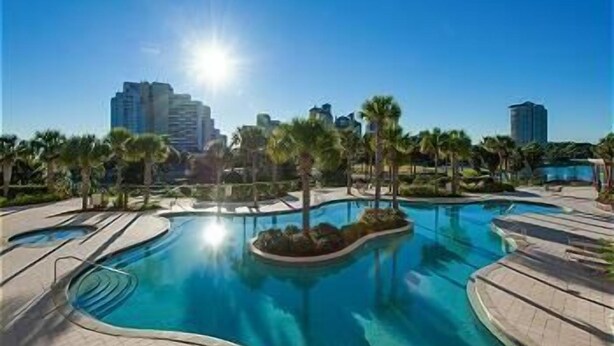 A swimming pool surrounded by palm trees and a city skyline. - Quaint Efficiency Suite-Sleeps 4-Resort Amenities (Miramar Beach)