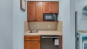 A compact kitchen with wooden cabinets, a built-in microwave, a stainless steel sink, and a dishwasher. - Quaint Efficiency Suite-Sleeps 4-Resort Amenities (Miramar Beach)
