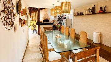 Un espace repas comprenant une table à plateau de verre, des chaises en bois, un four en briques et des lampes en osier suspendues.